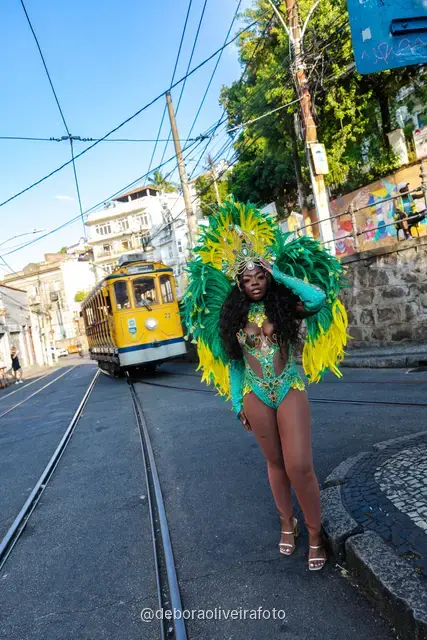 Mujer con disfraz de Carnaval de plumas verdes y amarillas junto al tranvía amarillo en Santa Teresa, Río de Janeiro
