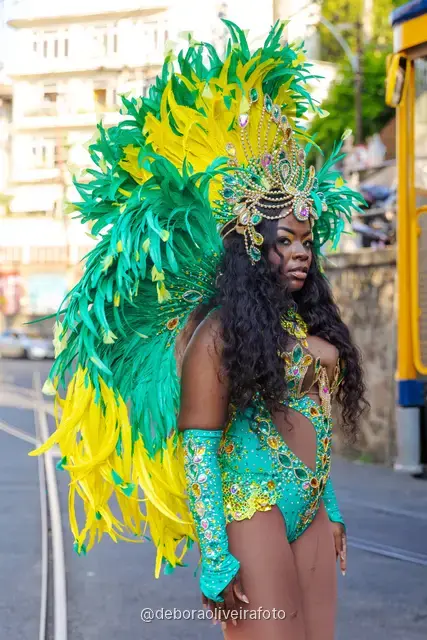Mujer con disfraz de Carnaval de plumas verdes y amarillas junto al tranvía amarillo en Santa Teresa, Río de Janeiro