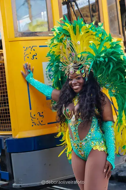Mujer con disfraz de Carnaval de plumas verdes y amarillas junto al tranvía amarillo en Santa Teresa, Río de Janeiro