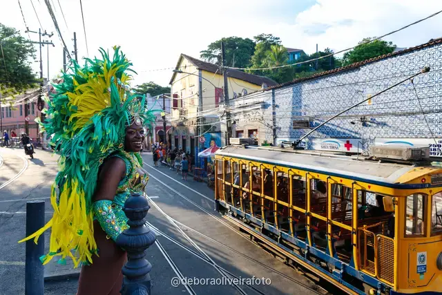 Retrato de cerca de un disfraz de Carnaval con plumas y tocado de pedrería frente a un mural colorido en Santa Teresa