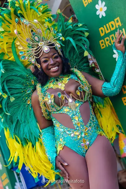 Woman in a Carnival costume walking on the street in Santa Teresa in front of a green wall and a mural with the tram and Sugarloaf