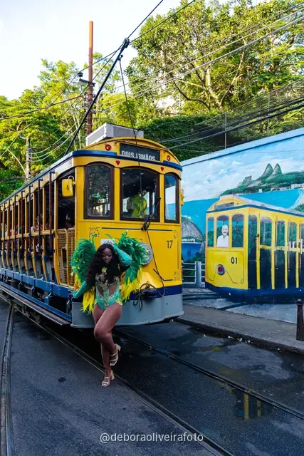 Mujer con disfraz de Carnaval caminando por la calle en Santa Teresa frente a una pared verde y un mural con el tranvía y el Pan de Azúcar