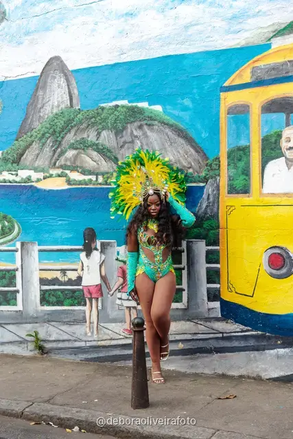Mujer con disfraz de Carnaval caminando por la calle en Santa Teresa frente a una pared verde y un mural con el tranvía y el Pan de Azúcar