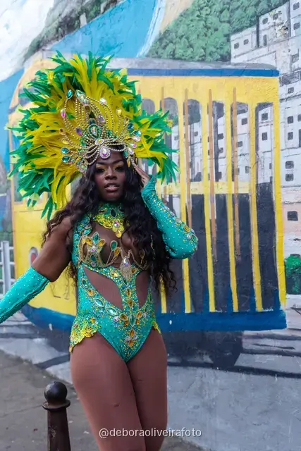 Mujer con disfraz de Carnaval caminando por la calle en Santa Teresa frente a una pared verde y un mural con el tranvía y el Pan de Azúcar