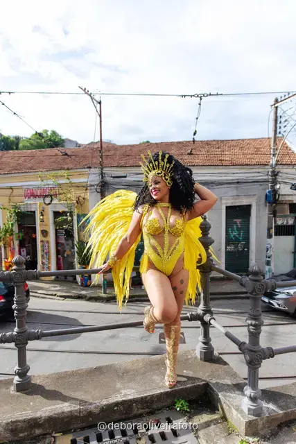 Mujer con disfraz de Carnaval amarillo frente a un mural con un tranvía amarillo y el Pan de Azúcar en Santa Teresa, Río de Janeiro