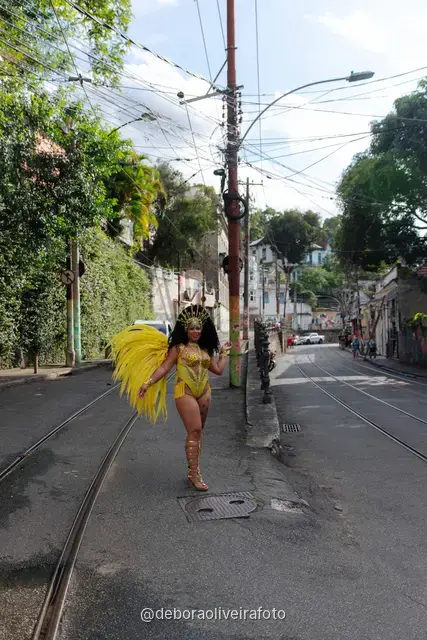 Mujer con disfraz de Carnaval amarillo frente a un mural con un tranvía amarillo y el Pan de Azúcar en Santa Teresa, Río de Janeiro