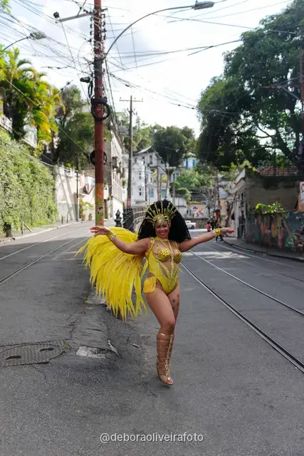 Mujer con disfraz de Carnaval amarillo frente a un mural con un tranvía amarillo y el Pan de Azúcar en Santa Teresa, Río de Janeiro