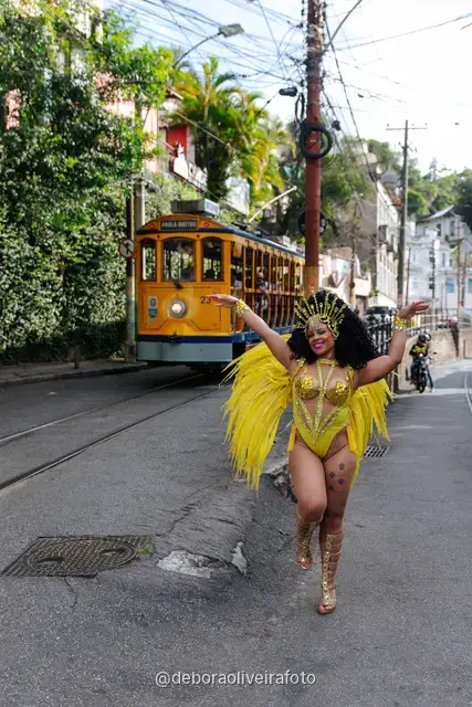 Mujer con disfraz de Carnaval amarillo frente a un mural con un tranvía amarillo y el Pan de Azúcar en Santa Teresa, Río de Janeiro