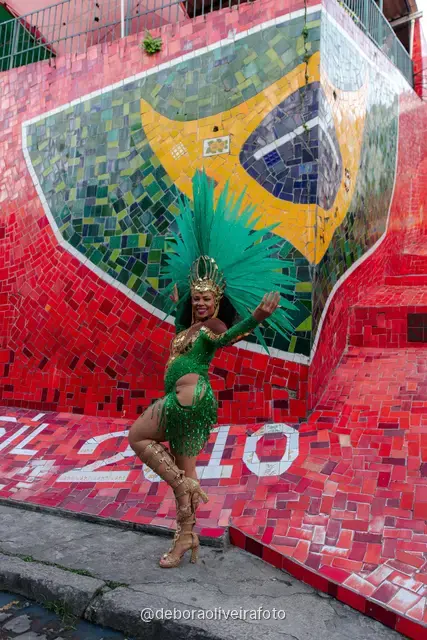Mujer con look verde de lentejuelas y tocado de plumas turquesa en la Escalinata Selarón y las paredes de azulejos rojos, en Río de Janeiro