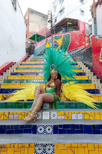 Mujer con look verde de lentejuelas y tocado de plumas turquesa en la Escalinata Selarón y las paredes de azulejos rojos, en Río de Janeiro
