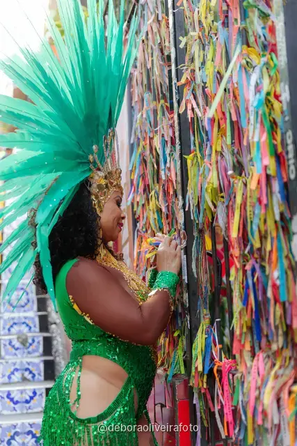 Mujer con disfraz de Carnaval verde y tocado turquesa junto a la pared de cintas de colores cerca de la Escalinata Selarón