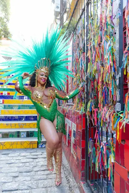 Mujer con disfraz de Carnaval verde y tocado turquesa junto a la pared de cintas de colores cerca de la Escalinata Selarón