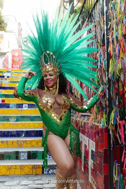 Mujer con disfraz de Carnaval verde y tocado turquesa junto a la pared de cintas de colores cerca de la Escalinata Selarón