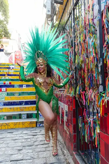 Mujer con disfraz de Carnaval verde y tocado turquesa junto a la pared de cintas de colores cerca de la Escalinata Selarón