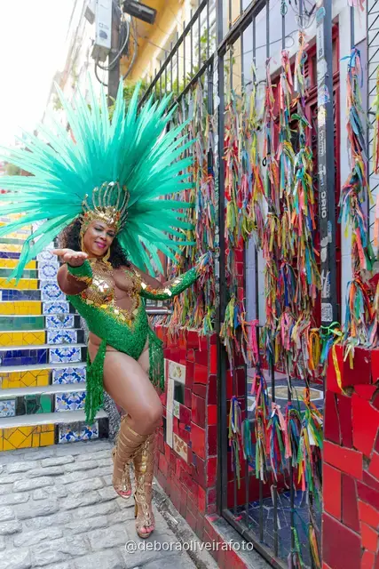 Mujer con disfraz de Carnaval verde y tocado turquesa junto a la pared de cintas de colores cerca de la Escalinata Selarón