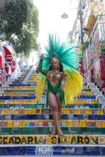 Mujer con disfraz de Carnaval verde y tocado turquesa junto a la pared de cintas de colores cerca de la Escalinata Selarón