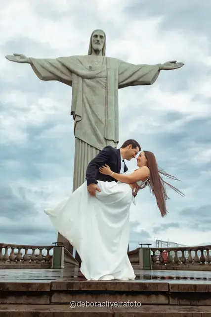 Couple in a white dress and a dark suit embracing at the foot of the Christ the Redeemer statue in Rio de Janeiro