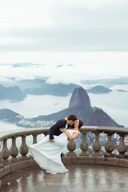 Couple walking and dancing on the Christ the Redeemer viewpoint with Sugarloaf Mountain and the bay behind