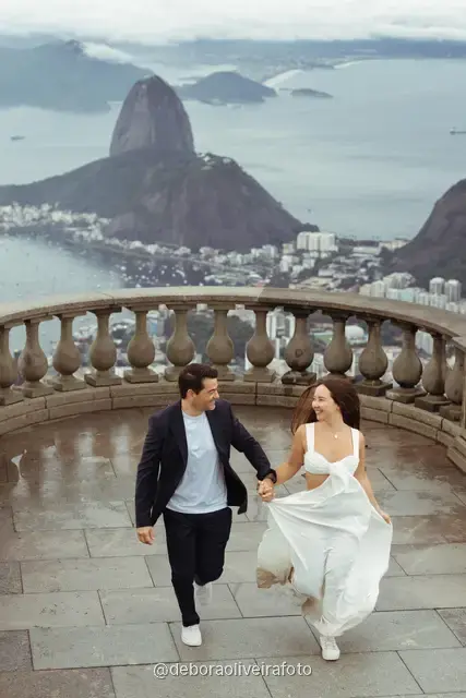 Couple walking and dancing on the Christ the Redeemer viewpoint with Sugarloaf Mountain and the bay behind