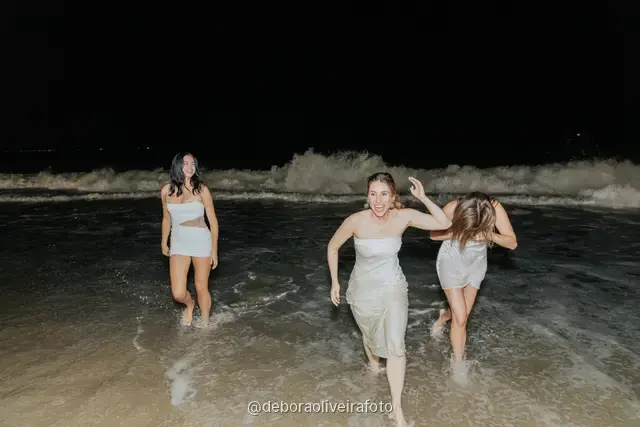 Group of women in white outfits running into the waves at Copacabana Beach at night in Rio de Janeiro