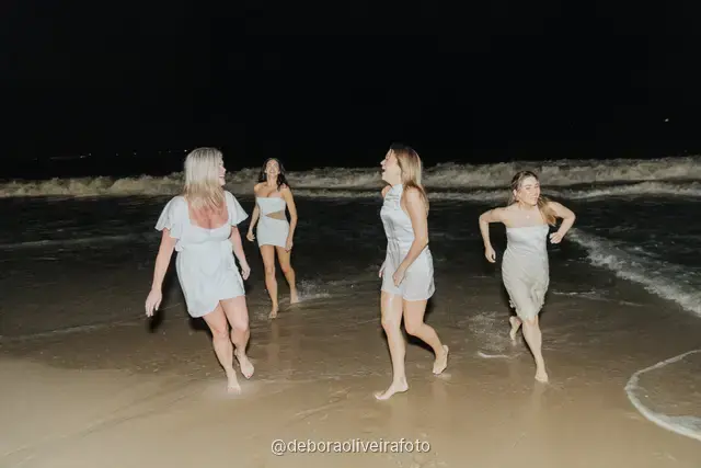 Grupo de mulheres de branco correndo nas ondas da praia de Copacabana à noite, no Rio de Janeiro
