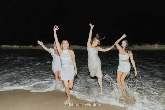 Group of four women in white jumping and posing together at Copacabana Beach at night