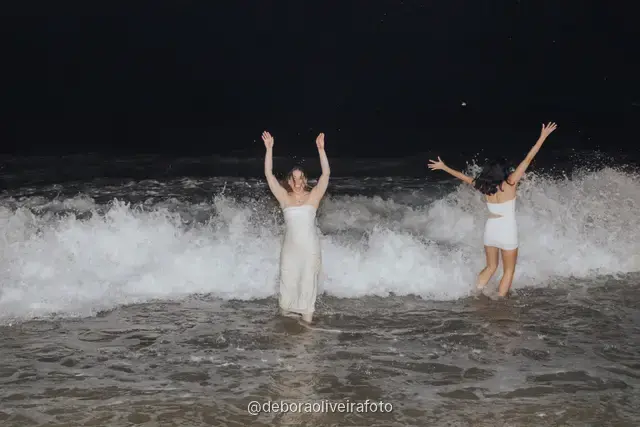 Grupo de mulheres de branco em pé nas ondas da praia de Copacabana à noite