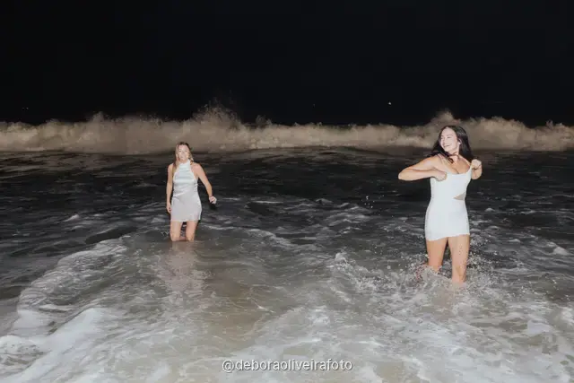 Grupo de mulheres de branco em pé nas ondas da praia de Copacabana à noite