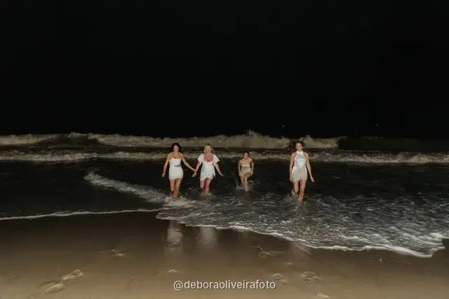 Grupo de mulheres de branco em pé nas ondas da praia de Copacabana à noite