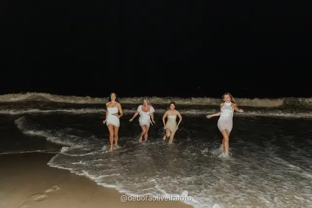 Grupo de mulheres de branco em pé nas ondas da praia de Copacabana à noite