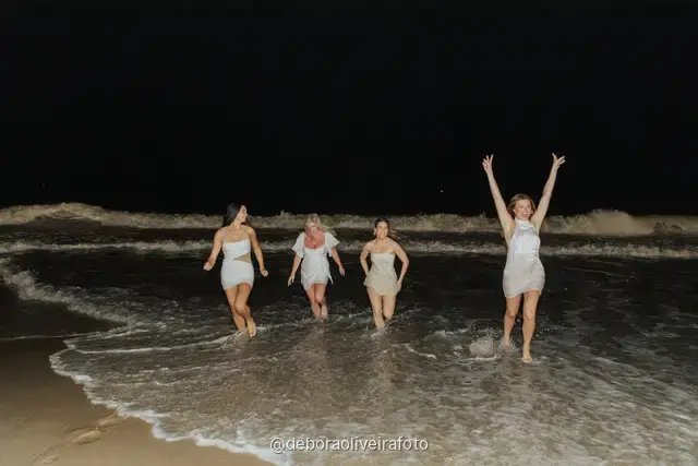 Grupo de mulheres de branco em pé nas ondas da praia de Copacabana à noite