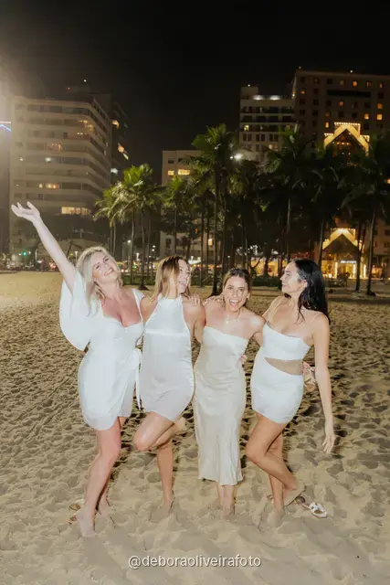Group of four women in white posing on the sand at Copacabana with the city lights behind at night