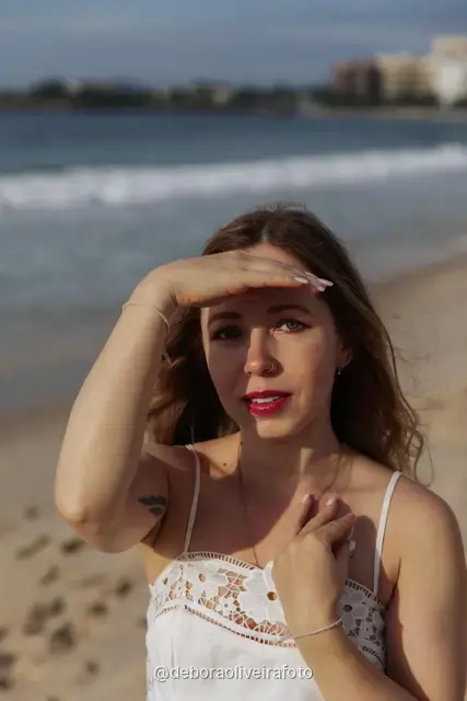 Woman in a white lace dress and green jacket sitting on the sand of Copacabana Beach