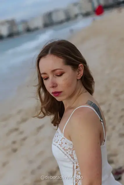 Woman in a white lace dress and green jacket sitting on the sand of Copacabana Beach