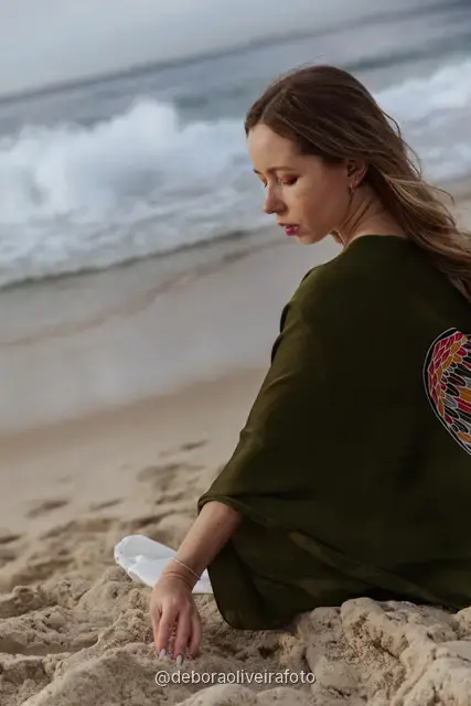 Woman in a white lace dress and green jacket sitting on the sand of Copacabana Beach