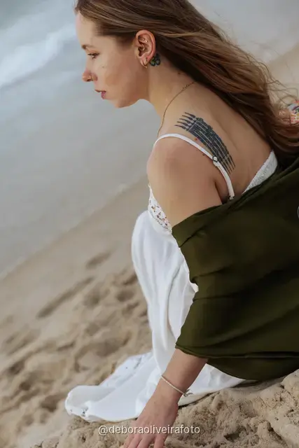 Woman in a white lace dress and green jacket sitting on the sand of Copacabana Beach