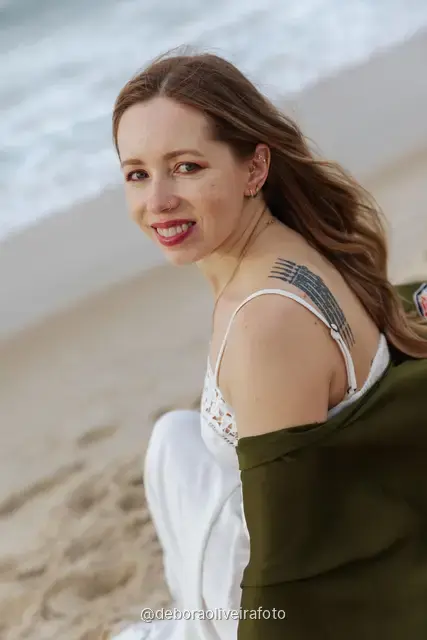 Woman in a white lace dress and green jacket sitting on the sand of Copacabana Beach