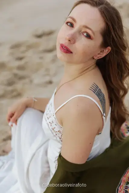 Woman in a white lace dress and green jacket sitting on the sand of Copacabana Beach