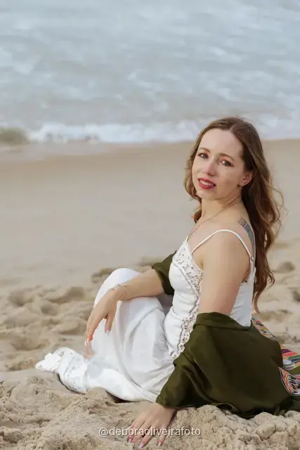 Woman in a white lace dress and green jacket sitting on the sand of Copacabana Beach