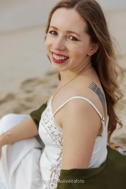Woman in a white lace dress and green jacket sitting on the sand of Copacabana Beach