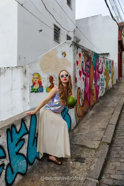 Woman in a sequin top in front of the red tile wall at the Selarón Steps, and a green coconut on a graffiti street corner