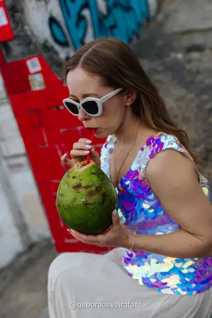 Woman in a sequin top in front of the red tile wall at the Selarón Steps, and a green coconut on a graffiti street corner