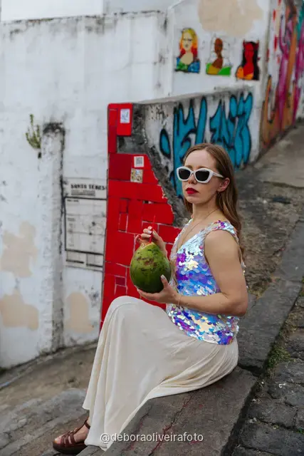 Woman in a sequin top in front of the red tile wall at the Selarón Steps, and a green coconut on a graffiti street corner