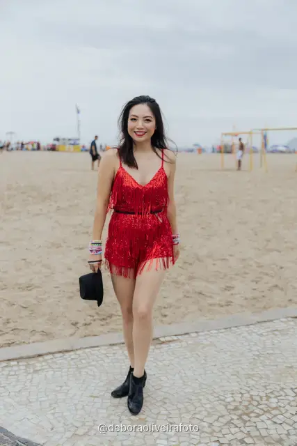 Woman in a red fringe romper with a hat and red sunglasses on the wave-pattern sidewalk of Copacabana in Rio de Janeiro