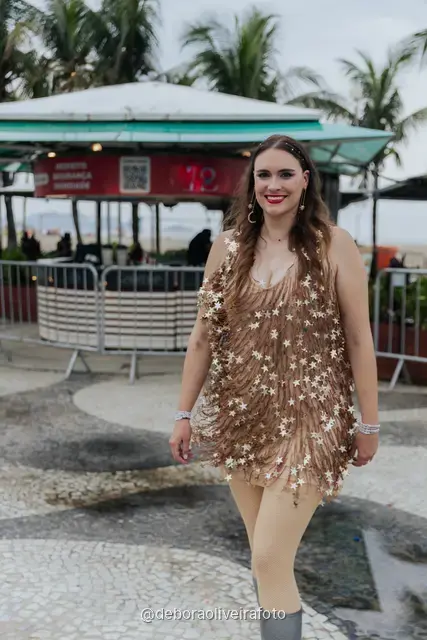 Persona con look de lentejuelas plateado y dorado junto a una palmera en la arena de Copacabana, en Río de Janeiro