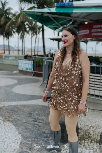 Person in a silver and gold sequin outfit next to a palm tree on the sand at Copacabana, Rio de Janeiro