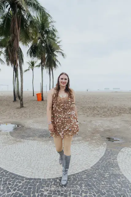 Persona con look de lentejuelas plateado y dorado junto a una palmera en la arena de Copacabana, en Río de Janeiro
