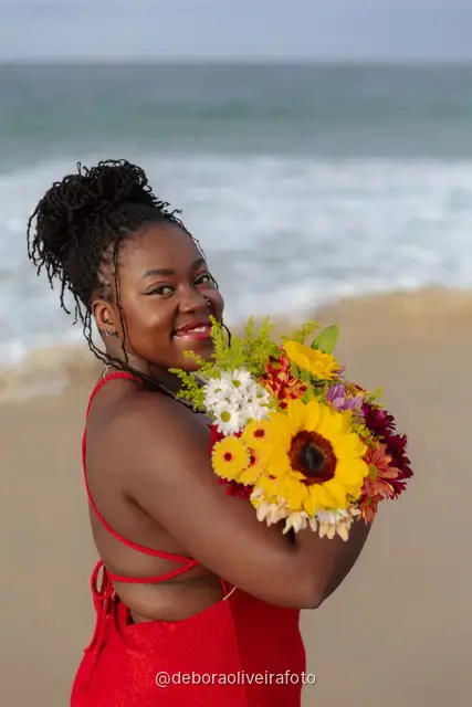Woman in a long red dress holding a bouquet of sunflowers at the water line of Ipanema Beach in Rio de Janeiro