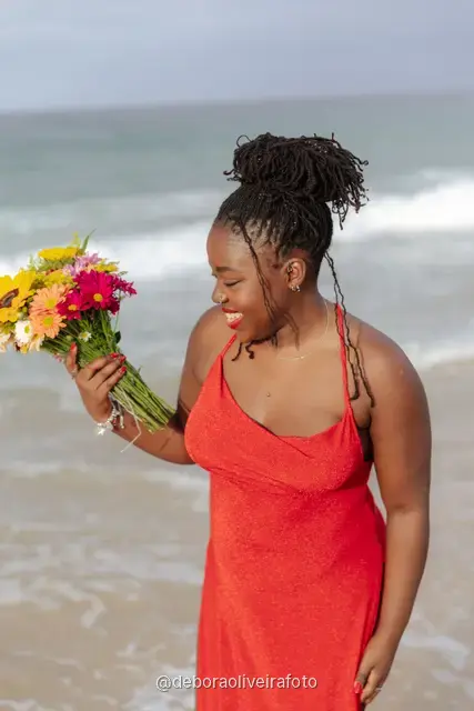 Woman in a long red dress holding a bouquet of sunflowers at the water line of Ipanema Beach in Rio de Janeiro