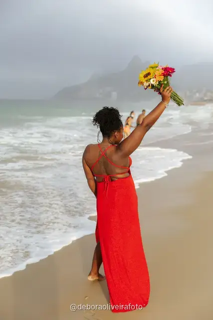 Woman in a long red dress holding a bouquet of sunflowers at the water line of Ipanema Beach in Rio de Janeiro